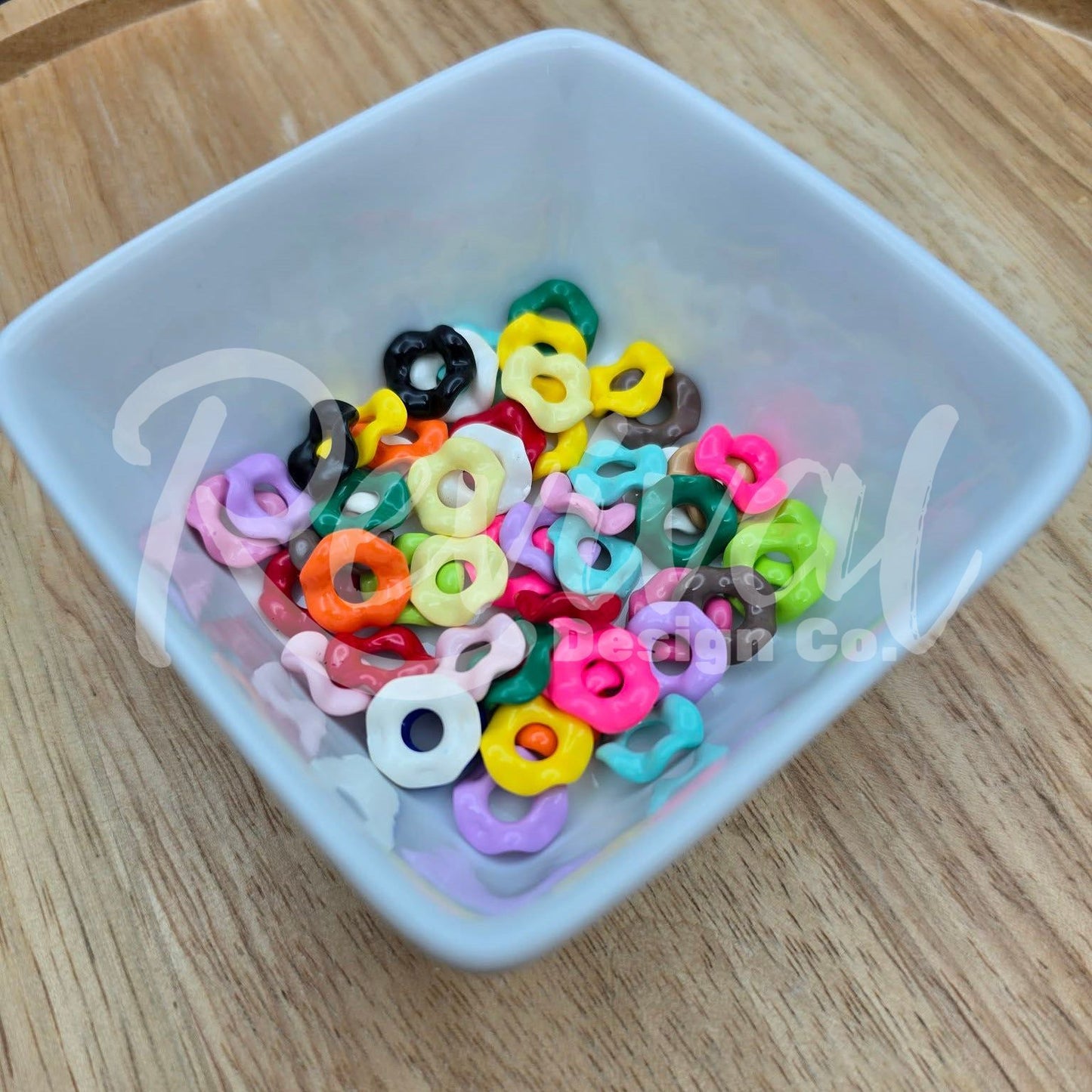 Colorful acrylic beads in a white bowl on a wooden surface