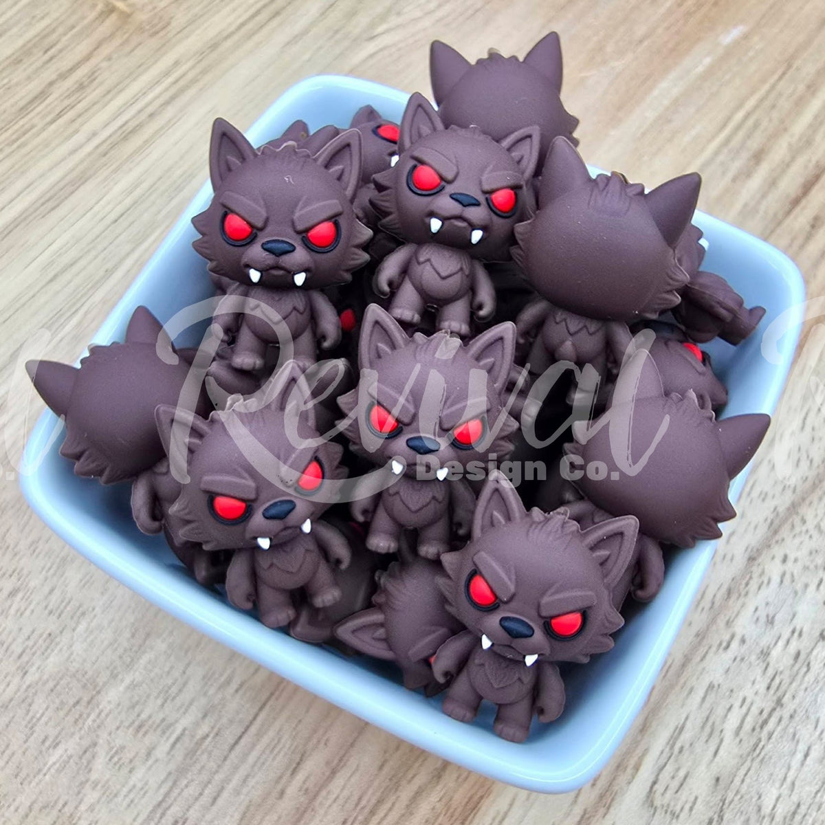 A group of small dark brown cartoon wolf figurines with glowing red eyes and white fangs, arranged in a light blue square dish on a light wood surface.