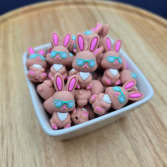 Small rabbit-shaped beads with sunglasses on a wooden surface