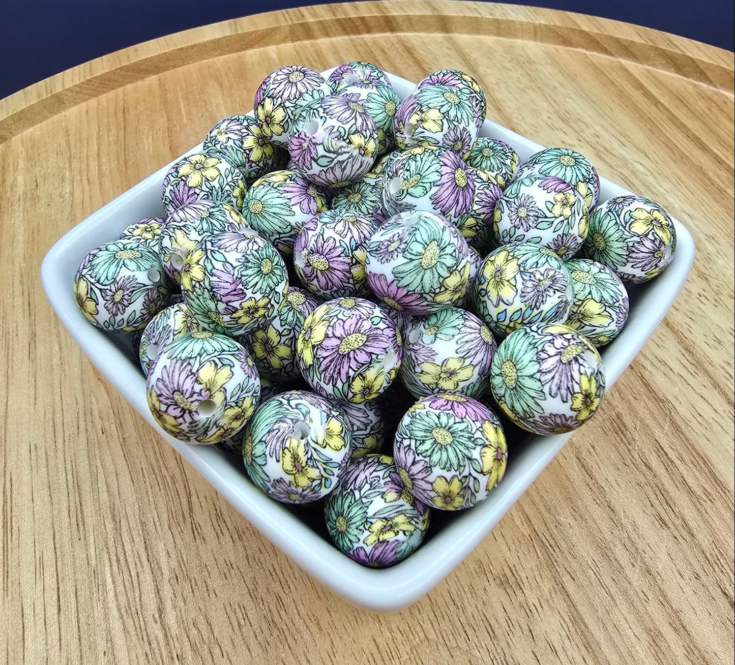 Decorative balls with floral patterns in a white bowl on a wooden surface