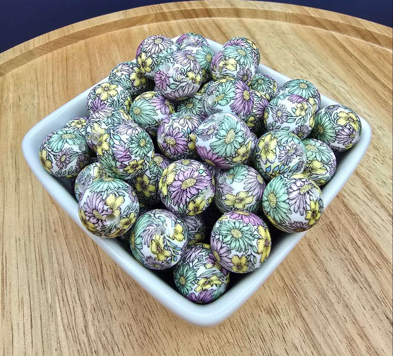 Decorative balls with floral patterns in a white bowl on a wooden surface