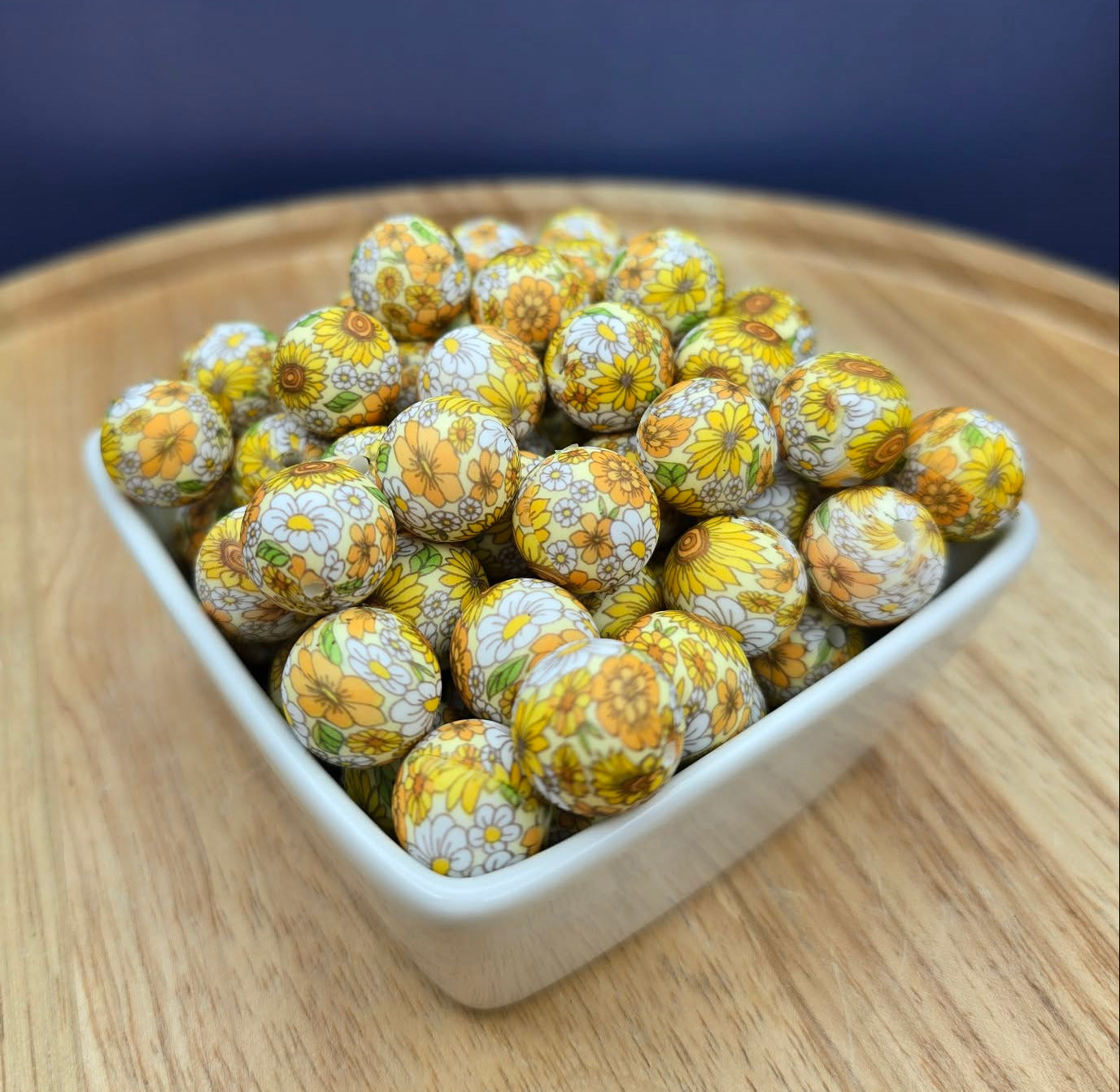 White container filled with yellow and white spherical beads on a wooden surface with a dark blue background
